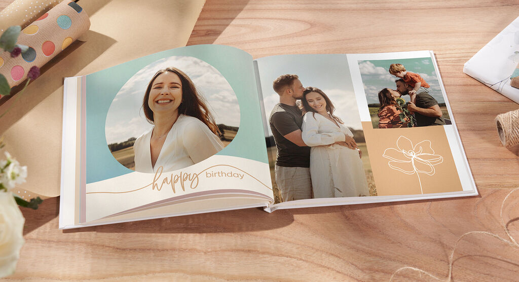 Ein offenes CEWE FOTOBUCH mit zwei liebevollen Bildern, einer Geburtstagsbotschaft und einem floralen Design.