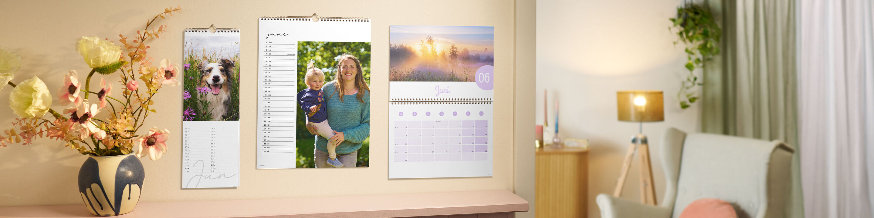 Drei CEWE Foto-Terminkalender hängen nebeneinander an einer Wand. Ein Hundefoto, ein fröhlicher Outdoor‑Moment und eine Morgenlandschaft.