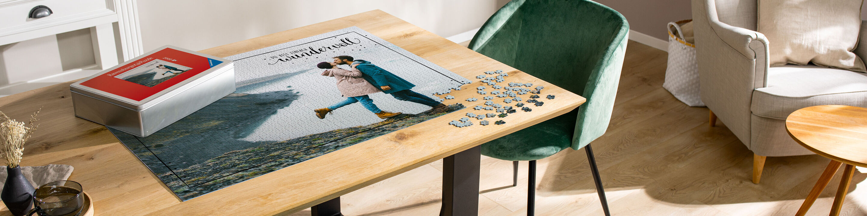 Ein CEWE FOTOBUCH liegt auf einem Holzschreibtisch. Der Tisch ist modern und schön eingerichtet. Auf dem Tisch sind Puzzlestücke verteilt und ein grüner Stuhl steht neben dem Tisch.