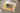 Auf einem Sofa liegt ein geschlossenes CEWE FOTOBUCH neben einem Kuscheltier und einer Decke. Auf dem Buchcover ist das Foto von drei kleinen Kindern abgebildet, die auf einer Wiese liegend nach oben in die Kamera lächeln. Der Titel lautet «Für Oma». Ein gelber Aquarellfleck und florale Elemente bilden den Hintergrund der Titelseite.