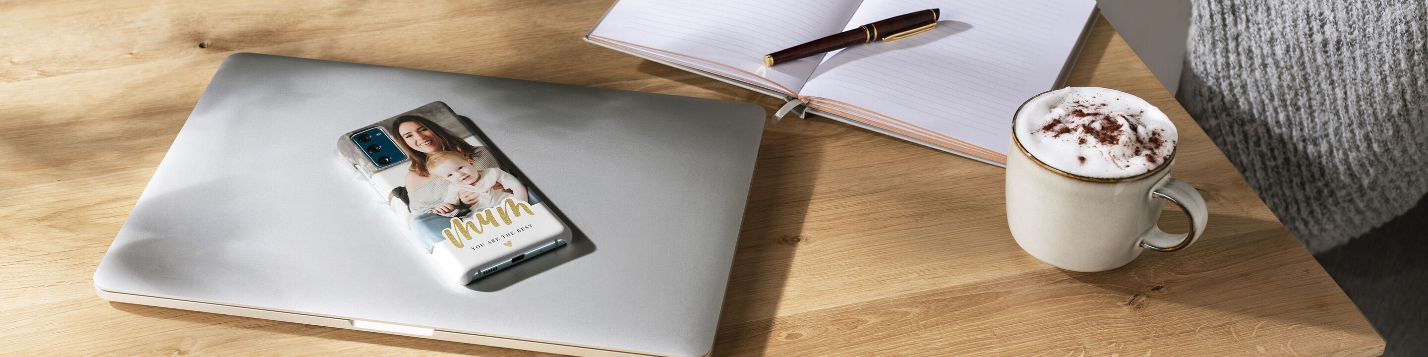 Eine Tasse mit Schokolade steht neben einemLaptop, auf dem ein CEWE Fotobuch liegt