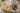 Auf einem Sofa liegt ein geöffnetes CEWE FOTOBUCH neben einem Kuscheltier und einer Decke. Auf der linken Seite ist das Foto einer Hand zu erkennen, die eine Kinderzeichnung von einer Familie festhält. Die Überschrift lautet «Wir fünf». Auf der rechten Seite ist ein Familienfoto mit den Eltern und drei Kindern zu sehen. Der Hintergrund der Doppelseite ist mit einem violetten Aquarellfarbverlauf gestaltet.