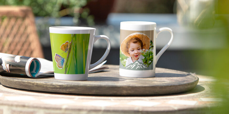 Zwei kreative Tassen mit bunten Designs und persönlichem Bild.
