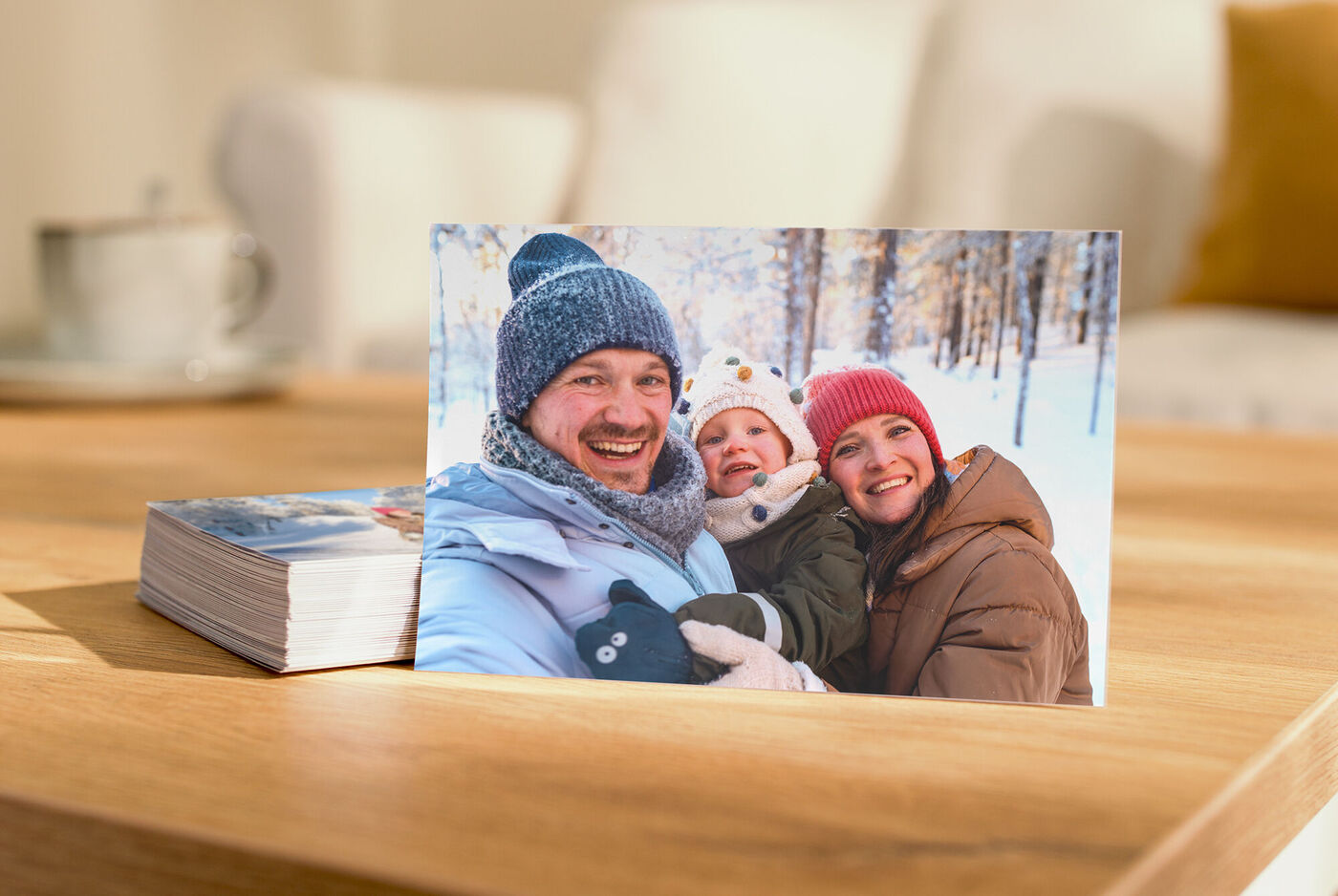 Ein gedrucktes Foto zeigt eine warm gekleidete Familie in einem winterlichen Wald; dahinter liegt ein Stapel weiterer Fotos.