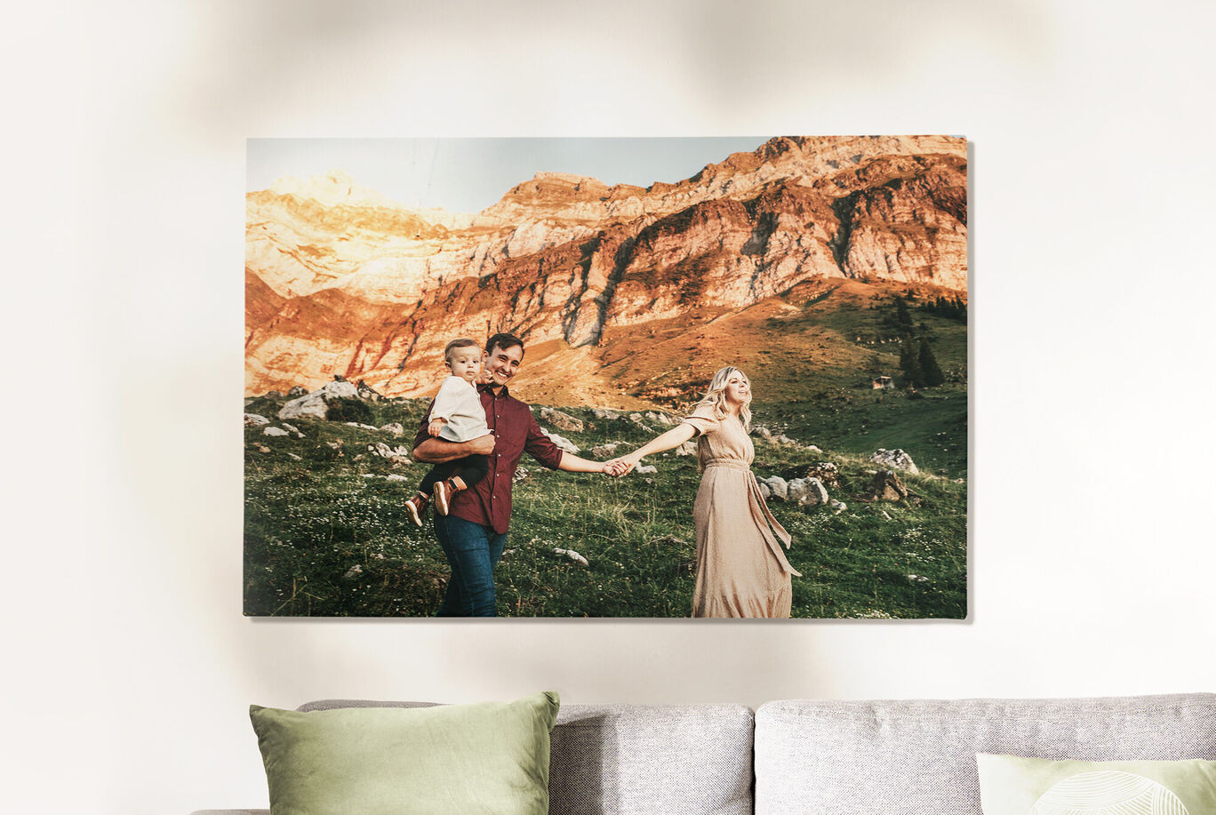 Eine Familie mit einem Kind in den Arme hält Händchen, während sie durch eine grüne Berglandschaft spaziert.