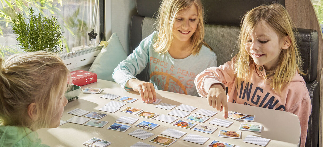 Drei Kinder spielen ein Erinnerungs-Spiel mit vielen Karten auf einem Tisch.