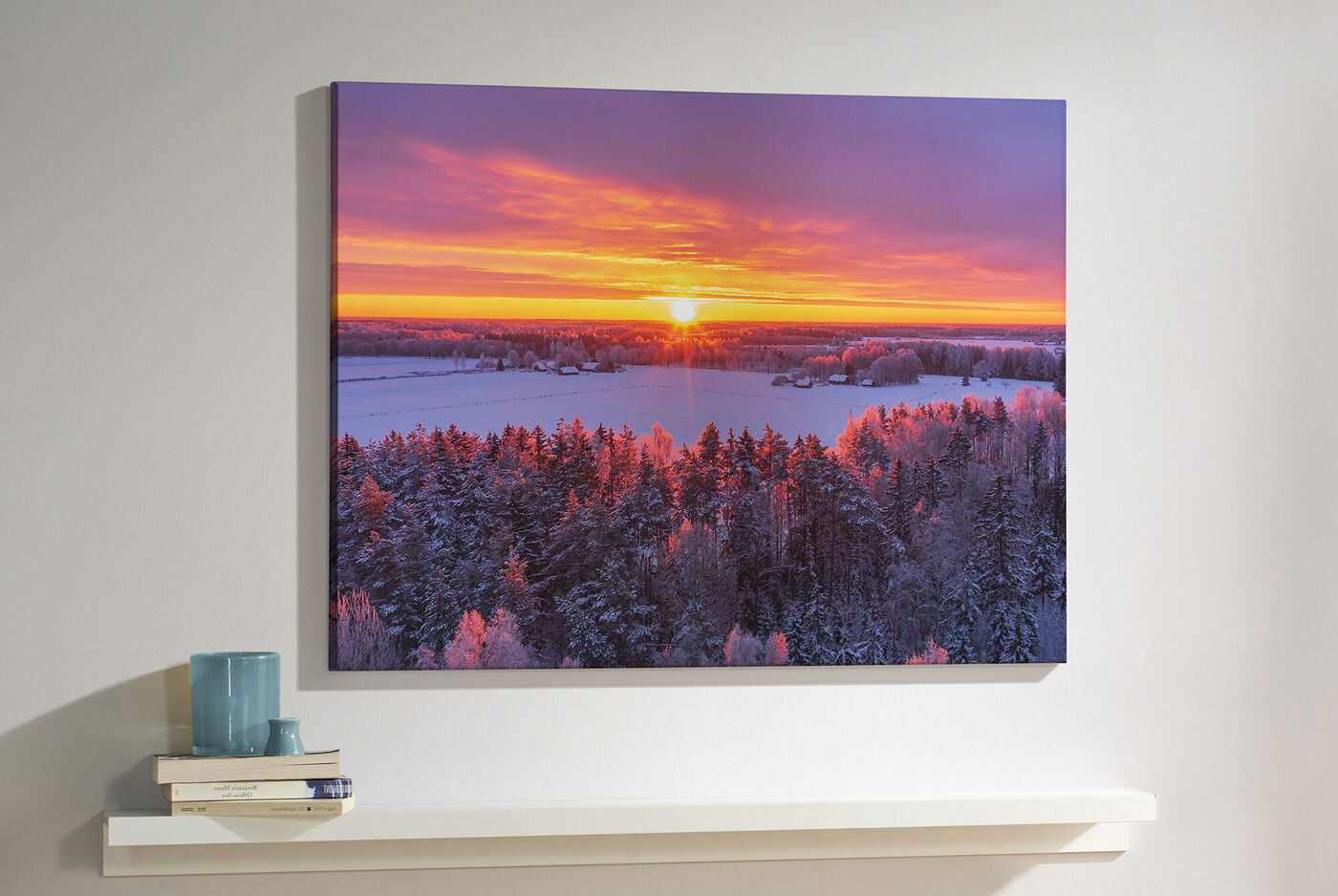 Ein CEWE Wandbild zeigt eine winterliche Landschaft mit schneebedecktem Wald und einem farbenfrohen Sonnenaufgang.