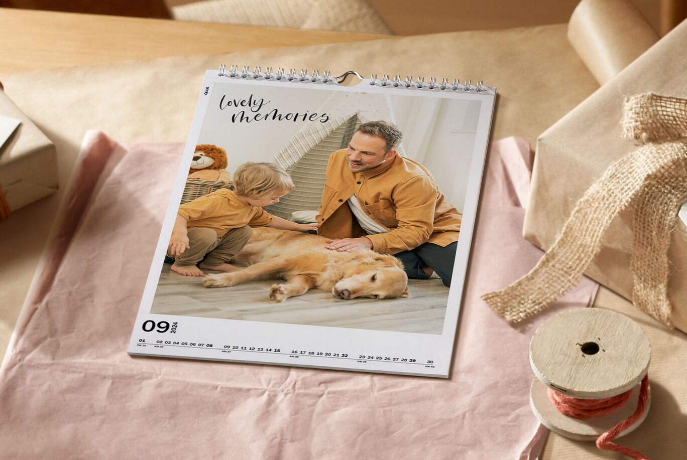 Ein Familienkalender auf einem Tisch. Darauf liegen ein Kind und ein Hund, während ein Erwachsener ihnen Gesellschaft leistet. Der Monat ist September.