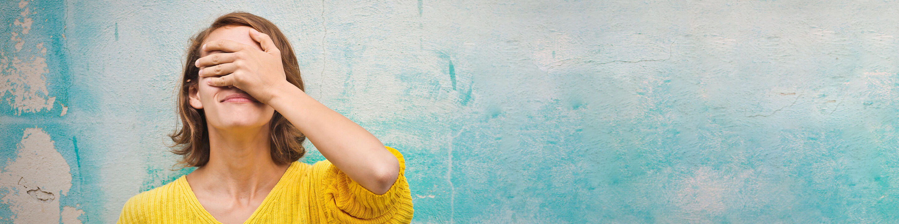 Eine Frau in einem gelben Pullover genießt einen Moment der Ruhe vor einer blauen Wand.