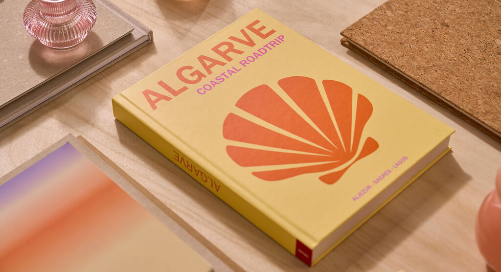 Auf einem Tisch liegt ein CEWE FOTOBUCH. Das Cover ist hellgelb und mit dem Schriftzug „Algarve“ gestaltet.